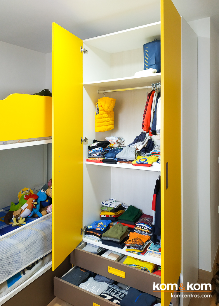 armario ropero de habitaci&oacute;n infantil color amarillo y marr&oacute;n chocolate. Esta abierto y se ve el interior lleno de ropa.
